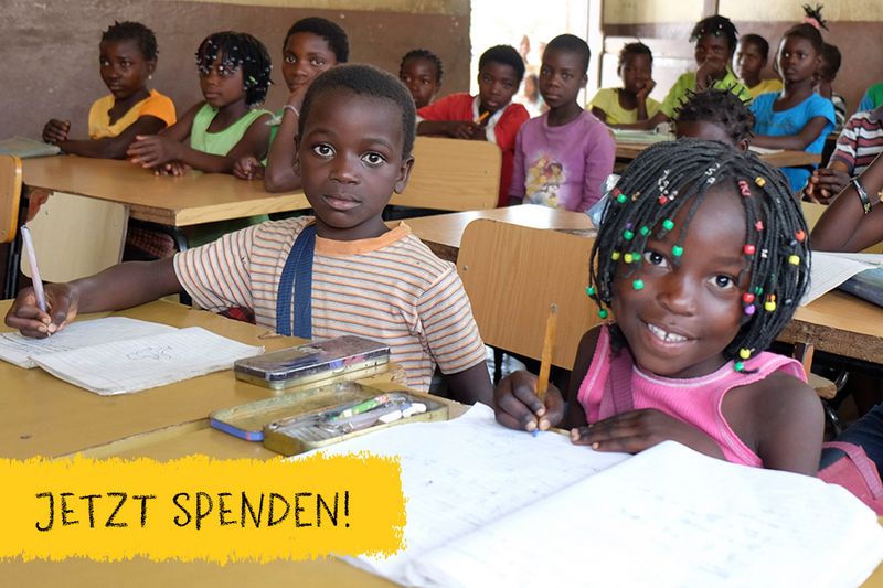 Ines sitzt mit einem Klassenkameraden in der Klasse am Tisch. Beide haben Hefte aufgeschlagen und Stifte in der Hand und sind froh darüber lernen zu dürfen.