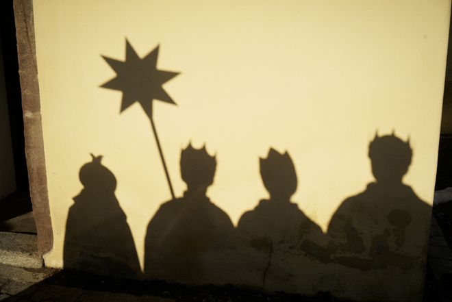 Der Schattenwurf einer Sternsingergruppe auf einer Hauswand. Der Schatten ist gestochen scharf und es sind sogar die Umhänge, Kronen und der Stern gut zu erkennen.