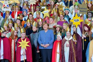 Bundeskanzlerin Angela Merkel in Mitten vieler Sternsinger. Die Sternsinger kommen aus ganz Deutschland und haben ihr eUmhänge und Kronen an. Auf den Sternen steht woher die Sternsinger kommen. 