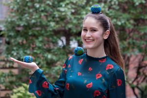 Die Freiwillige Isabel aus Aachen. Sie Balanciert drei Bähe. Einen auf dem Kopf, einen auf der rechten Schulter und einen auf der offenen Handfläche. Sie trägt ein dunkel grünes Kleid mit roten Blumen. 