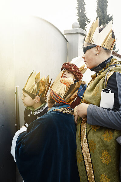 Neugierig schauen die Sternsinger durch ein Gartentor. Einer der Jungen trägt eine dunkle Brille.