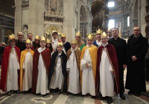 14 Sternsinger sind zusammen mit Prälat Krämer im Petersdom. Die Sternsinger haben Umhänge und Kronen an. Im Hintergrund sieht man die beeindruckende Kunstfertigkeit und die diesen Ausmaße die den Petersdom ausmachen.