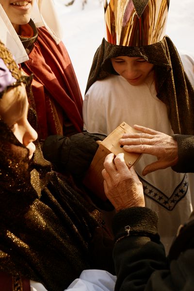 Drei Sternsinger halten eine Spendenbox. Eine Person für die gesungen wurde wirft etwas Geld in die Spendenbox. Die Sternsinger mit Kronen und Gewändern freuen sich darüber.