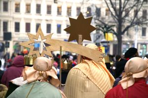 Vier Sternsinger gehen in einem Wohngebiet von Haus zu Haus. Sie tragen den Stern, Kronen und leuchtende bunte Gewänder und Umhänge.