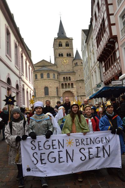 Sternsingerzug mit mehr als 2.659 Sternsingern zieht durch die Innenstadt von Trier. Prälat Dr. Klaus Krämer, Präsident des Kindermissionswerks ,Die Sternsinger', Dr. Stephan Ackermann, Bischof von Trier, und Pfarrer Dirk Bingener, Bundespräses des Bundes der Deutschen Katholischen Jugend gehen gemeinsam mit den Kindern voran. Die Sternsinger tragen einen Banner mit dem Slogan der Sternsinger voran. Der Slogan lautet Segen bringen, Segen sein. Im Hintergrund ist das Trierer Münster.