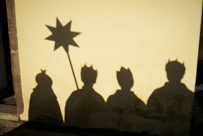 Der Schattenwurf von vier Sternsingern an einer Wand. Man erkennt den gezackten Stern und die unterschiedlich geformten Kronen. 
