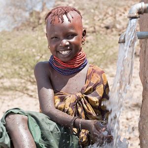 Aweet an einem Brunnen mit frischem Wasser. Sie lächelt und ist glücklich über die Wasserquelle.