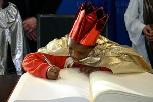 Der Sternsinger Emmanuel Traor aus Duttlenheim trägt sich in das goldene Buch des Europaparlaments ein. Er trägt einen goldenen Umhang und hat eine rote Krone auf dem Kopf. Er schreibt grade sehr konzentriert in das goldene Buch.