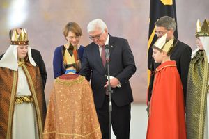 Der Bundespräsident zusammen mit seiner Frau und vier Sternsingern. Die Sternsinger haben bunte festliche Gewänder an. Sie tragen auch goldene Kronen auf dem Kopf. Prälat Krämer steht in der nähe der Sternsinger.