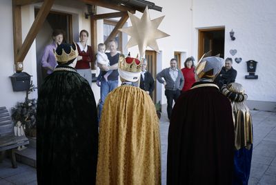 Eine Familie hört aufmerksam den Sternsinger beim Singen zu. Die Sternsinger haben Umhänge und Kronen an und tragen den Stern vor sich.