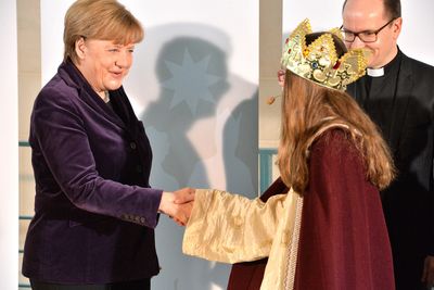 Bundeskanzlerin Angela Merkel begrüßt eine Sternsingerin indem sie ihr die Hand schüttelt.