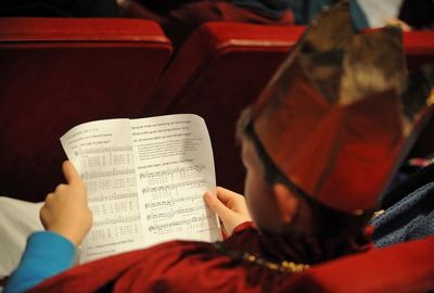 Ein Sternsinger sitzt in einer Kirchenbank und liest sich den Text zur Segnung der Kreide durch. 