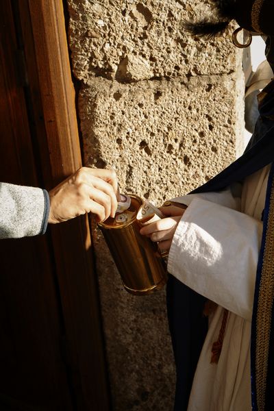 Ein Sternsinger bekommt von einer anderen Person Geld in die goldenen Spendenbox geworfen. 