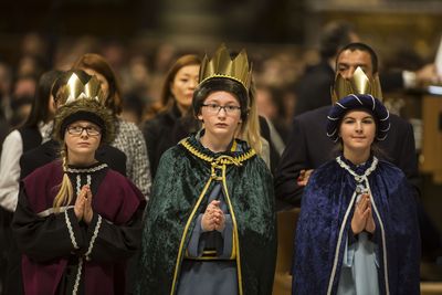 Drei Sternsinger beim Gebet im Petersdom. Sie haben an der Gabenprozession mitgewirkt und tragen die Sternsingergewänder. Zusätzlich haben sie goldene Kronen auf dem Kopf. die Die Sternsinger haben andächtig die Hände vor der Brust gefaltet.