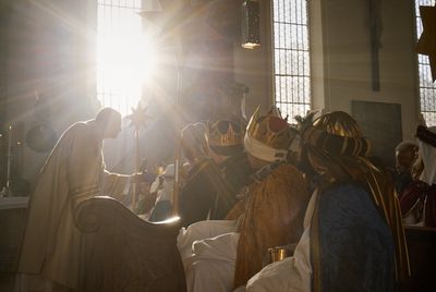 Sternsinger wohnen einem Gottesdienst bei. Die Sternsinger sitzen und er ersten Reihe und der Priester geht herum und segnet die Sternsinger. Die Kinder haben aufwändige Kostüme und Kronen an.