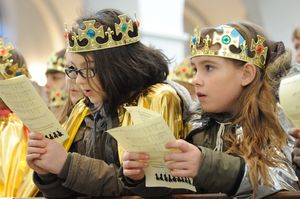 Sternsinger bei einer Zeremonie in einer Kirche. Sie haben Kronen und Gewänder an und halten Lidtexte vor sich. Die Sternsinger singen mit.