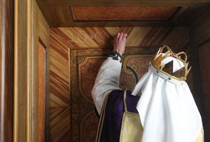 Ein Sternsinger mit Krone und Gewand schreibt den traditionellen Segen der Sternsinger, mit Kreide, an eine Haustür.