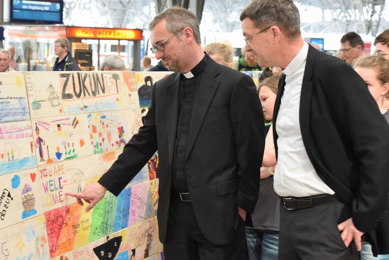 Erzbischof Dr. Stefan Heße, Sonderbeauftragter für Flüchtlingsfragen der Deutschen Bischofskonferenz und Prälat Dr. Klaus Krämer, Präsident Kindermissionswerk ‚Die Sternsinger‘, begucken in der Haupthalle des Leipziger Hauptbahnhofs das  symbolische Rettungsboot aus 1.000 bunten Planken.