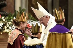 Drei Sternsinger stehen vor Papst Franziskus. Sie haben die traditionellen Gewänder an. Die Sternsinger haben an der Gabenprozession teilgenommen. Papst Franziskus Blick gütig auf die Sternsinger und berührt einen von ihnen an der Wange und lächelt. 