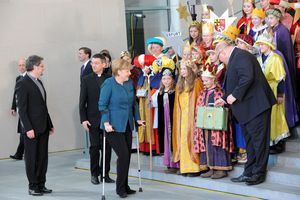 Bundeskanzlerin zusammen mit den Sternsinger die sch auf einer großen Treppe aufgestellt haben. Peter Altmeter übergibt einen kleinen Koffern eine Sternsingerin und Prälat Krämer geht hinter Angela Merkel her.