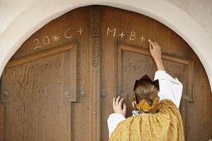 Ein Sternsinger schreibt den traditionellen Segen der Sternsinger an eine Haustür.