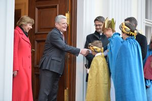 Bundespräsident Joachim Gauck und seine Frau begrüßen die Sternsinger im Schloss Bellevue. Die Sternsinger tragen bunte Umhänge und haben goldenen Kronen an. Der Bundespräsident Joachim Gauck reicht einem der Sternsinger die Hand und begrüßt ihn. 