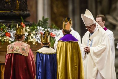 Drei Sternsinger stehen vor Papst Franziskus. Sie haben die traditionellen Gewänder an. Die Sternsinger haben an der Gabenprozession teilgenommen. Der Papst hat andächtig das Haupt gesenkt.