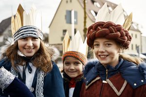 Lisa, Fabian und Clara lächeln als Sternsinger verkleidet in die Kamera.          