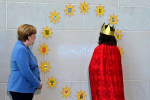 Eine Sternsingerin schreibt den Segensgruß an die Wand des Bundeskanzleramts zwischen die Sterne die kreisförmig an der Wand angebracht sind. Jeder Stern steht dabei für ein Bundesland aus denen die Sternsinger zu Gast gekommen sind.