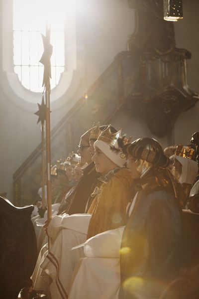 Sternsinger setzten in der ersten Reihe in der Kirche. Sie haben Gewänder und Kronen an. Im Hintergrund kann man noch das Inventar und die Verzierungen der Kirche erkennen.