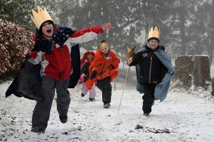 Dieser vierköpfige Sternsingergruppe läuft einen verschneiten Weg entlang. Sie tragen bunte Umhänge und goldene Kronen. Die Sternsinger sind voller Energie und freuen sich darüber, dass sie unterwegs sind.