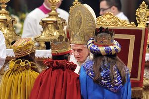 Drei Sternsinger empfangen den Segen von Papst Benedikt. Die Sternsinger haben ihre bunten Umhänge an und tragen goldene Kronen auf dm Kopf. Der Papst hat sich in seinem Stuhl etwas nach vorne gebeugt um besser mit den Sternsinger reden zu können. Papst Benedikt trägt sein volles Ornat. 
