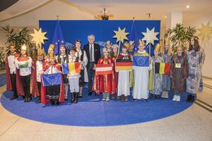 Der deutsch EU-Vizepräsident Rainer Wieland empfängt die Sternsinger. Es sind insgesamt dreiundzwanzig Sternsinger aus sechs Ländern. Die Sternsinger tragen bunte, festliche Gewänder und haben goldenen Krön auf dem Kopf. Außerdem haben sie drei Sterne dabei die sie an Stöcken der ihren Kopf halten. EU- Vizepräsident Rainer Wieland steht in der Mitte der Sternsingergruppe. 