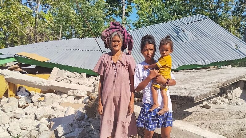 Drei Personen vor zerstörtem Gebäude in Indonesien nach dem Erdbeben