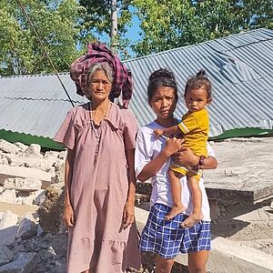 Drei Personen vor zerstörtem Gebäude in Indonesien nach dem Erdbeben