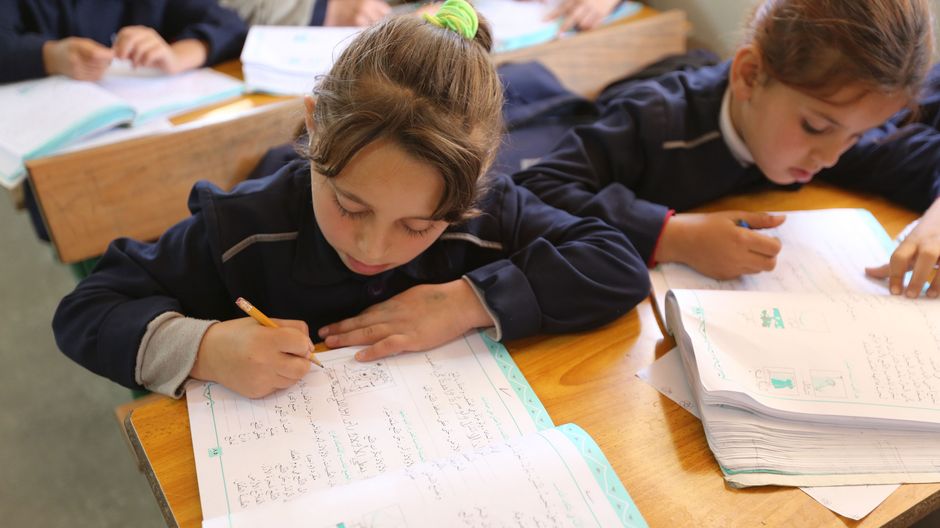 Khadija in der Schule. Neben Ihr sitzt die Klassenkameradin. Beide schreiben in Ihre Arbeitshefte und sind konzentriert.