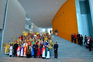 Die Bundeskanzlerin Angela Merkel und Prälat Krämer beim Gruppenfoto im Bundeskanzleramt. Die große Gruppe hat sich auf den Treppenstufen verteilt damit man auch alle auf dem Foto sehen kann.