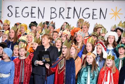 Die Bundeskanzlerin singt mit den vielen Sternsinger die sie umgeben. die Sternsinger haben Umhänge und Kronen auf.