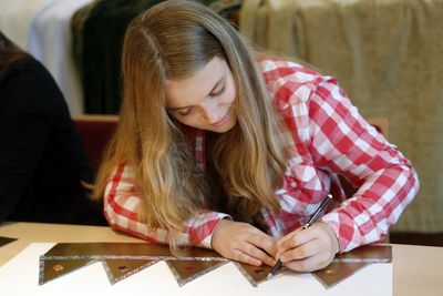 Die Sternsingerin Alina sitzt am Tisch und bastelt an ihrer Krone. Sie arbeitet an Verzierungen für ihrer Krone.