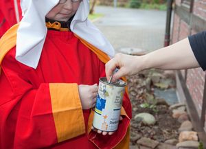 Ein Sternsinger in traditioneller Kleidung hält die Spendendose vor sich. Eine Person wirft etwas Geld als Spende hinein.