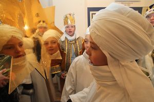 Zwei Sternsinger bei den letzten Vorbereitungen für die Sternsingeraktion. Sie tragen ihre traditionelle Kleidung und betrachten den goldenen Stern den sie an einem Stock befestigt haben. Der Stern glänzt so stark, dass sie ihn als Spiegel benutzen können. eine Gesichter spiegeln sich im Stern.