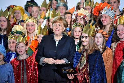 Die Bundeskanzlerin Angela Merkel inmitten vieler Sternsinger. Die Sternsinger singen gemeinsam und haben Umhänge und Kronen an.
