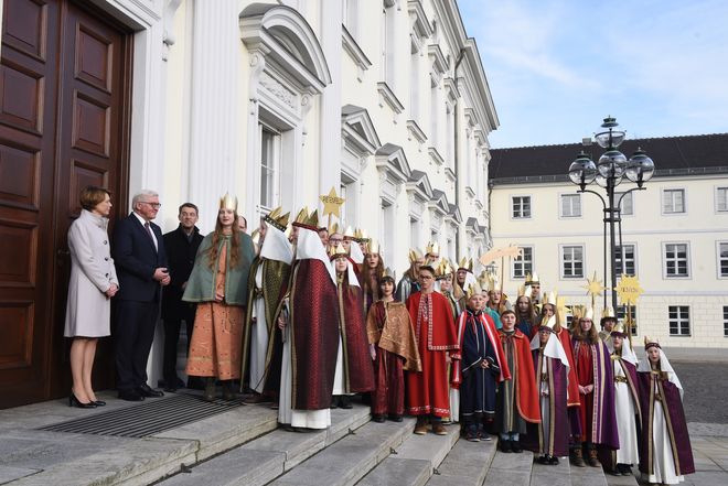 Bundespräsident Frank Walter Steinmeier und seine Frau begrüßen auf den Treppen des Schlosses Bellevue die Sternsinger die zusammen mit Prälat Krämer zu besuch gekommen sind. Sie Sternsinger haben die traditionellen Gewänder der Heiligen Drei Könige  und funkelnde Kronen an. Es sind mindestens 20 Sternsinger.