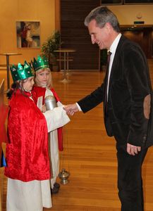 Der deutsche EU- Kommissar für Energie, Günther Öttinger empfängt die Sternsinger. Er steht vor zwei Sternsiegerinnen und reicht ihnen die Hand. Die Sternsinger haben ein Gefäß mit Weihrauch und eine Spendendose mit dabei. Die Sternsinger sind in rote umhänge gekleidet und haben Kronen auf dem Kopf. 