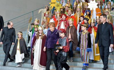 Bundeskanzlerin Angela Merkel geht zusammen mit den Sternsingern und dem Prälaten Krämer die Treppe im Bundeskanzleramt herunter. Sie unterhält sich mit einigen Sternsingern.