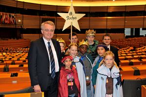 Vizepräsident des Europaparlaments Rainer Wieland führt die Sternsinger durch den Plenarsaal des Europaparlaments. Die Sternsinger tragen bunte Gewänder und haben goldenen Kronen auf dem Kopf. Sie sind beeindruckt von der Größe des Plenarsaals indem so viele wichtige Entscheidungen für viele Menschen getroffen werden