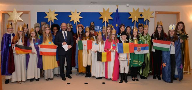 EU- Parlamentspräsident Martin Schulz empfängt Sternsinger aus sieben Ländern im EU- Parlament. Die Sternsinger halten Flaggen verschiedener Nationen vor sich. Sie tragen alle die traditionelle festliche Kleidung der Sternsinger. Das heißt sie tragen Umhänge und Kronen. Martin Schulz steht in der Mitte der Sternsingergruppe.