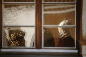 Ein Blick von draußen durch ein geschlossenes Fenster in ein Wohnzimmer hinein.  Die Sternsinger stehen in dem Zimmer und sind in warmes Licht getaucht. 