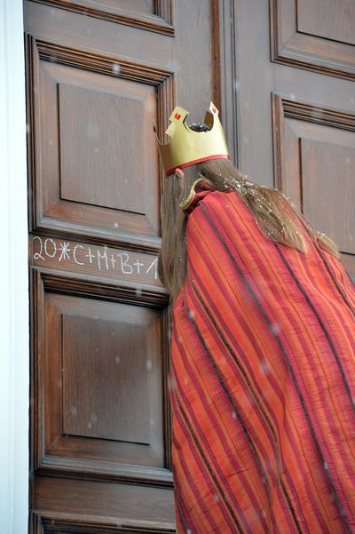 Eine Sternsingerin in einem dunkel rot und hell rot gestreiftem Umhang, schreit den Segen der Sternsinger an die Tür des Schlosses Bellevue. 