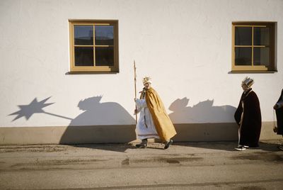 Eine Gruppe von Sternsinger auf dem Weg zur nächsten Station. Sie tragen den Stern vor sich her. Die Sonne wirft die Schatten der Drei an eine Hauswand.